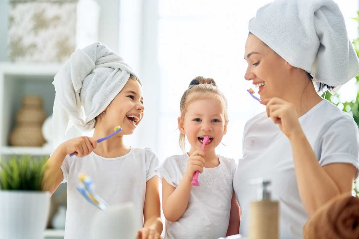 Juntas en el espejo: una madre enseña a sus hijas el valor de los buenos hábitos de higiene dental.